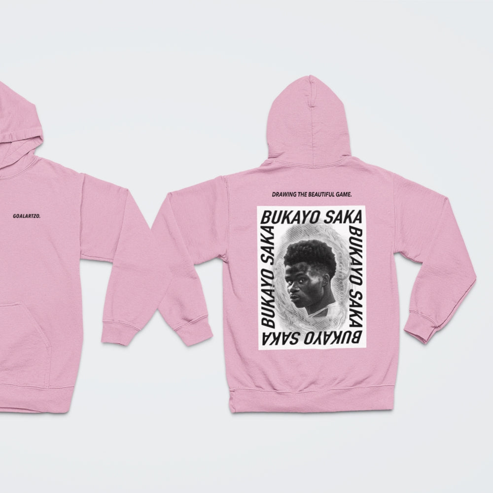 Baby Pink Arsenal Bukayo Saka hoodie by Goalartzo laying flat against a pale background. You can see both sides of the hoodie laid flat. There is a logo on the front chest reading 'goalartzo' and a large black and white graphic design featuring Bukayo Saka Art on the back.