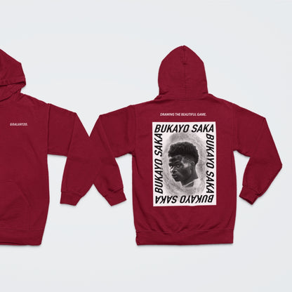 Deep Red Arsenal Bukayo Saka hoodie by Goalartzo laying flat against a pale background. You can see both sides of the hoodie laid flat. There is a logo on the front chest reading 'goalartzo' and a large black and white graphic design featuring Bukayo Saka Art on the back.