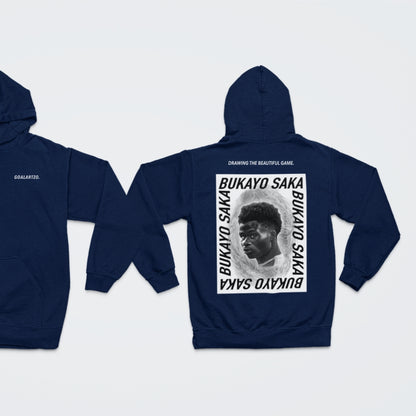 Dark Navy Blue Arsenal Bukayo Saka hoodie by Goalartzo laying flat against a pale background. You can see both sides of the hoodie laid flat. There is a logo on the front chest reading 'goalartzo' and a large black and white graphic design featuring Bukayo Saka Art on the back.