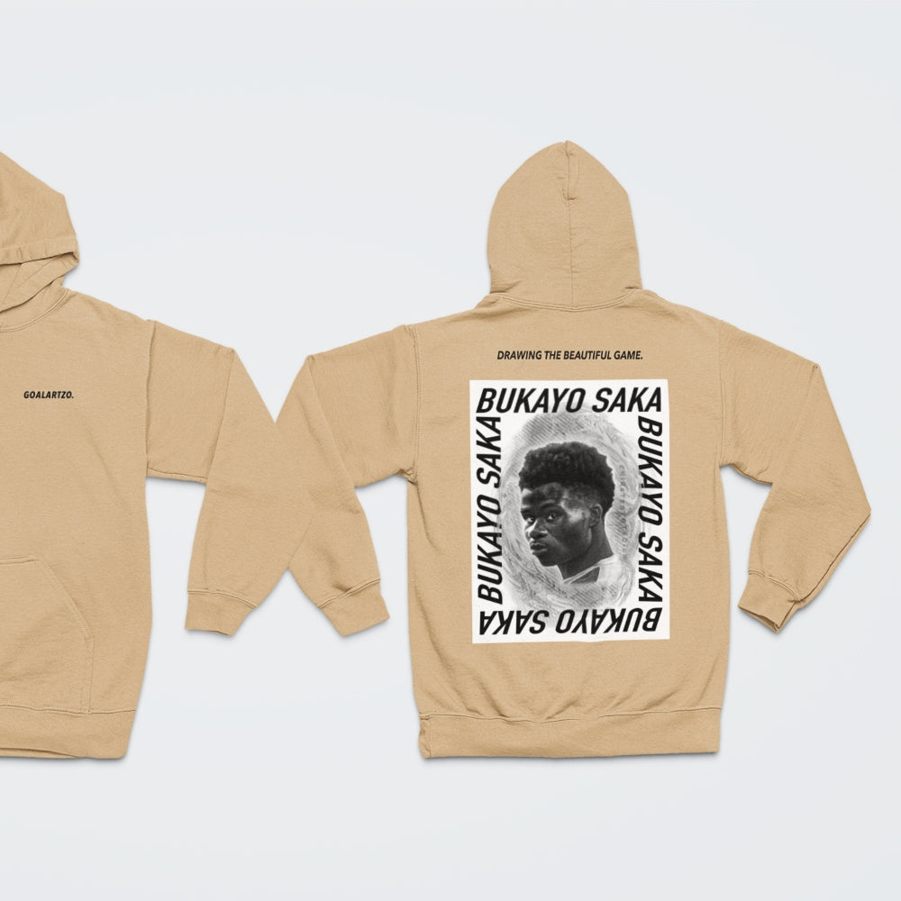 Nude, sand coloured Arsenal Bukayo Saka hoodie by Goalartzo laying flat against a pale background. You can see a logo on the front chest reading 'goalartzo' and a large black and white graphic design featuring Bukayo Saka Art on the back.