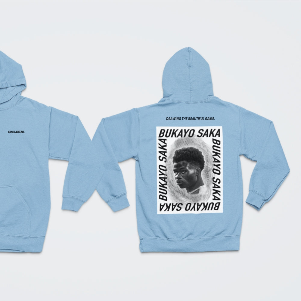 Sky Blue Arsenal Bukayo Saka hoodie by Goalartzo laying flat against a pale background. You can see both sides of the hoodie laid flat. There is a logo on the front chest reading 'goalartzo' and a large black and white graphic design featuring Bukayo Saka Art on the back.