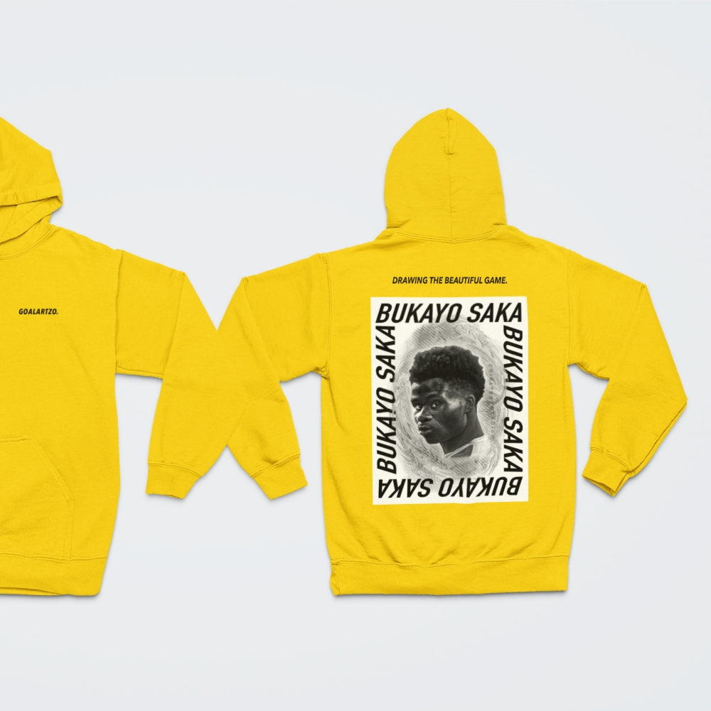 Bright Yellow Arsenal Bukayo Saka hoodie by Goalartzo laying flat against a pale background. You can see both sides of the hoodie laid flat. There is a logo on the front chest reading 'goalartzo' and a large black and white graphic design featuring Bukayo Saka Art on the back.